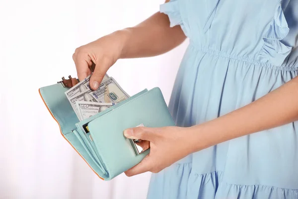 Woman taking out cash from stylish wallet on light background, closeup
