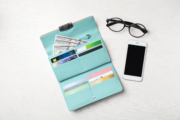 Smartphone, glasses and stylish wallet with cash and credit cards on light background, top view