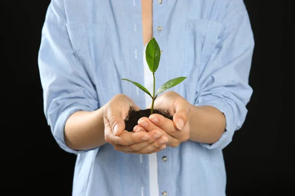 在黑色背景下手持绿色植物的妇女拿着土壤 — 图库照片