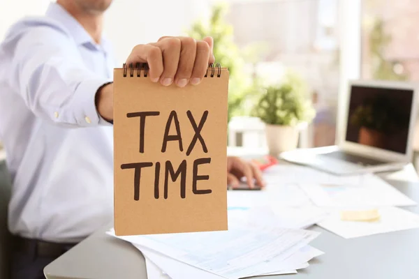 Homem Segurando Notebook Com Palavras Tax Tempo Dentro Casa — Fotografia de Stock