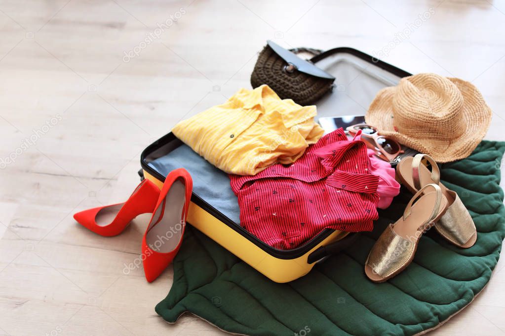 Open suitcase with clothes and accessories on floor