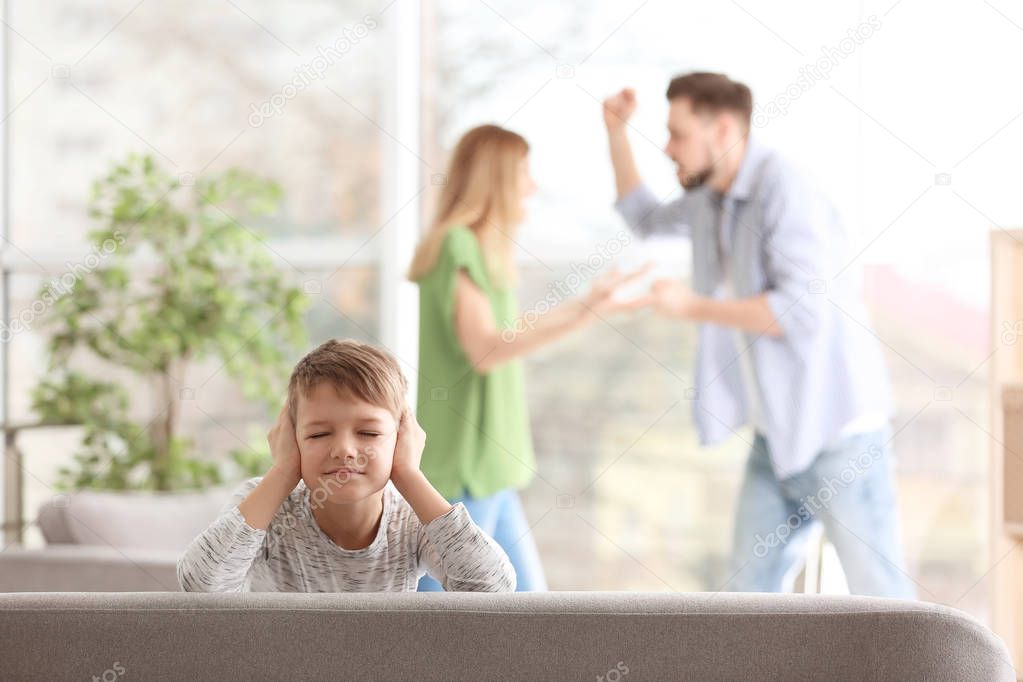 Little unhappy boy sitting on sofa while parents arguing at home