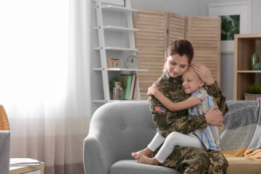 Woman in military uniform with her little daughter on sofa at home clipart