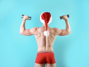Noel Baba şapkası renk arka plan üzerinde dumbbells ile genç kaslı adam