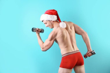 Noel Baba şapkası renk arka plan üzerinde dumbbells ile genç kaslı adam