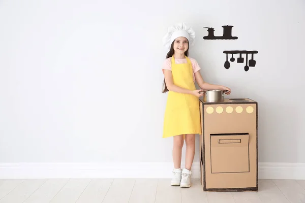 Little child in chef hat playing with carton stove indoors