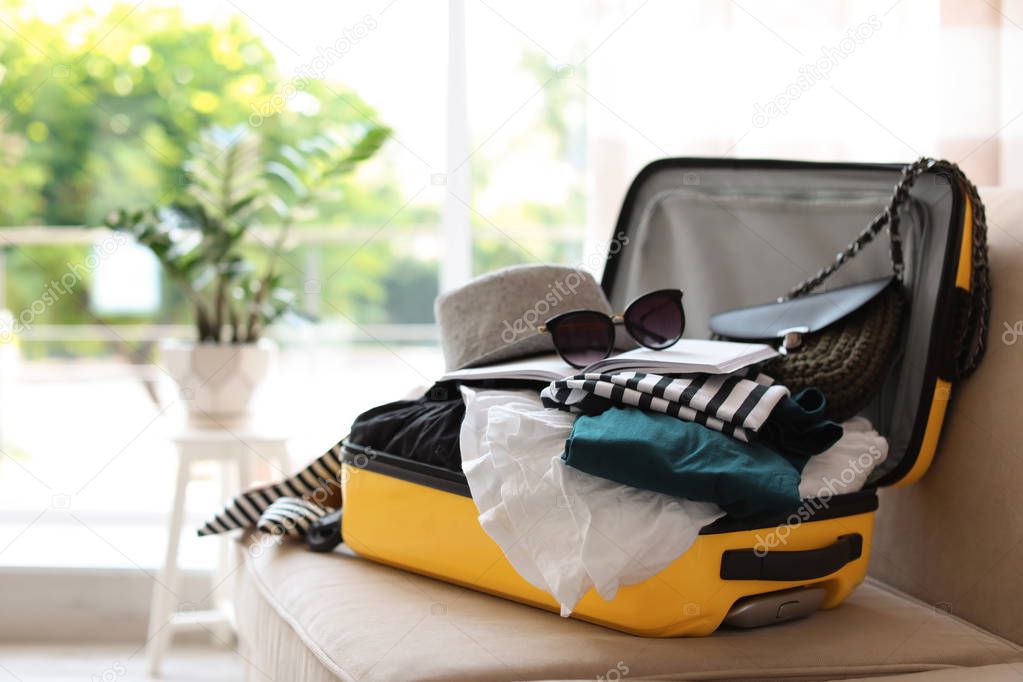 Open yellow suitcase with different clothes packed for journey at home