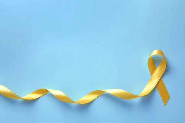 Yellow ribbon on color background, top view. Cancer awareness