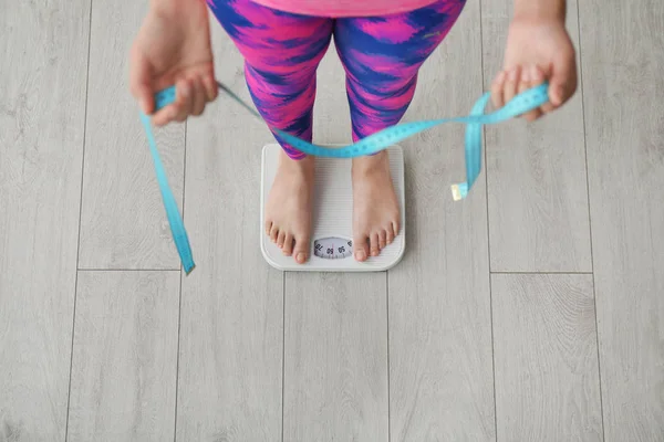 Woman with tape measuring her weight using scales on floor, top view. Healthy diet