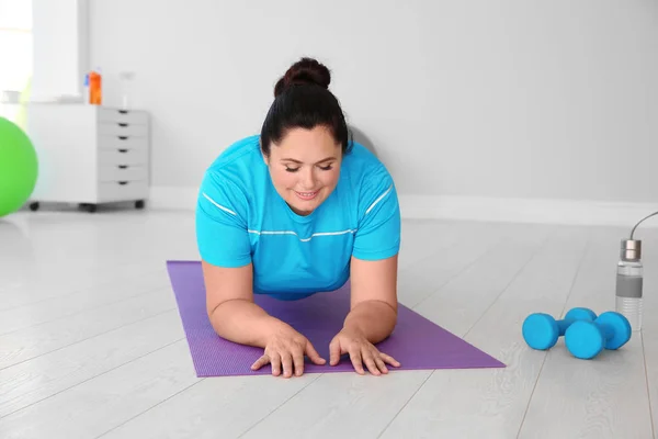 Overweight woman doing plank exercise on mat in gym