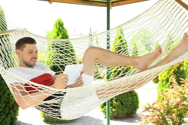 Adam açık havada sıcak yaz gününde hamakta rahatlatıcı tablet ile