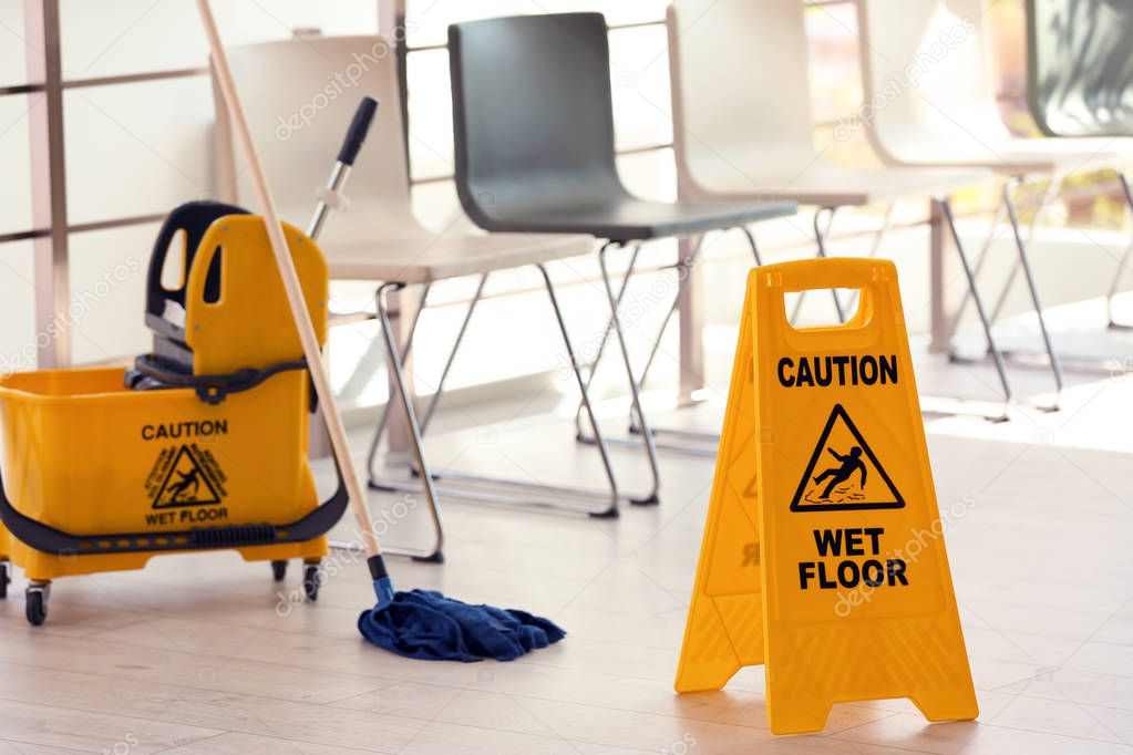 Safety sign with phrase Caution wet floor and mop bucket, indoors. Cleaning service