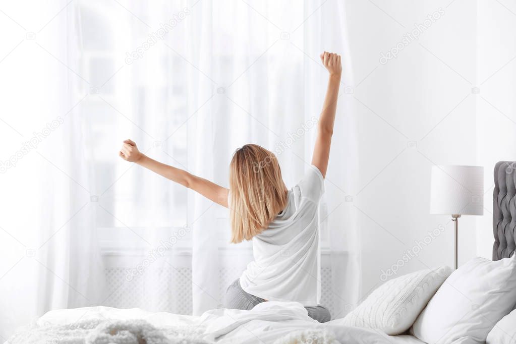 Young beautiful woman stretching after sleeping on bed at home