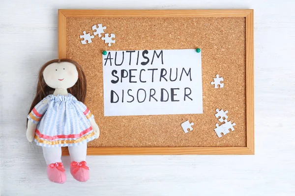 Sheet of paper with words AUTISM SPECTRUM DISORDER and doll on cork board