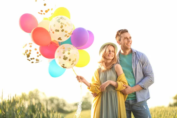 阳光明媚的日子 年轻的情侣带着五颜六色的气球在田野上 — 图库照片