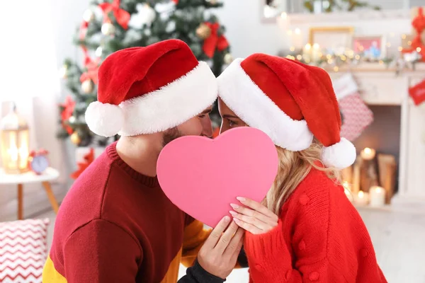 Młoda Para Santa Kapelusze Chowając Się Serce Domu Boże Narodzenie — Zdjęcie stockowe