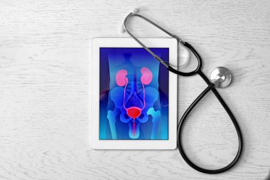 Tablet displaying urinary system and stethoscope on wooden background. Urology concept clipart