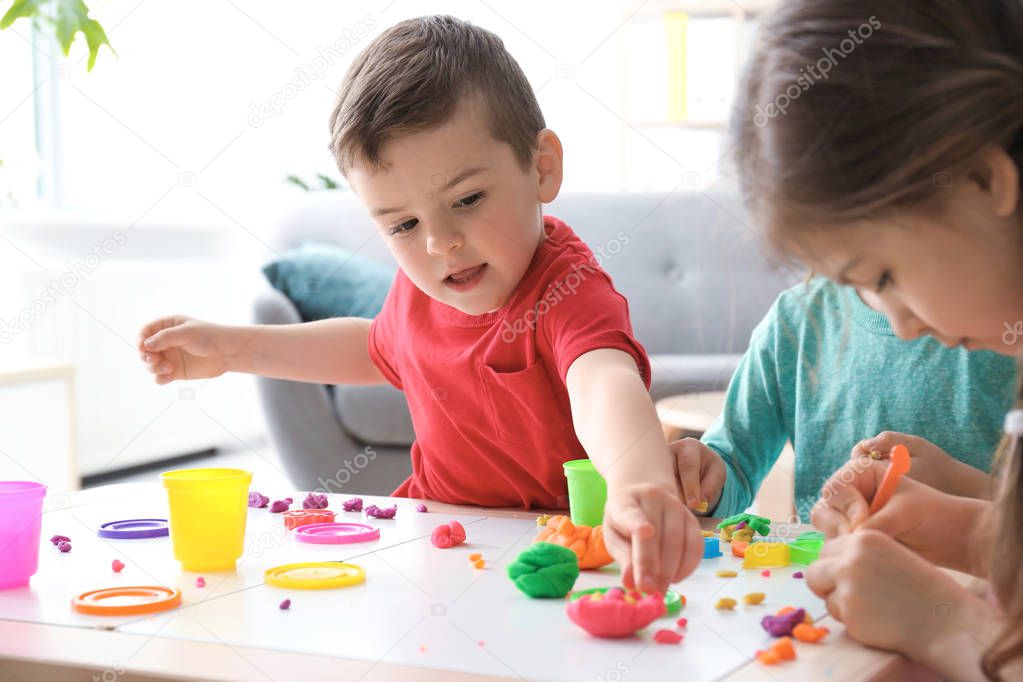 Cute little children using play dough at table indoors