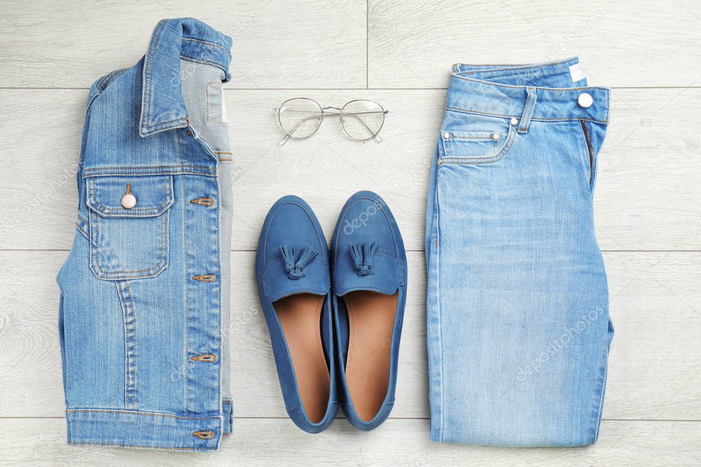 Flat lay composition with blue jeans, jacket and shoes on wooden background