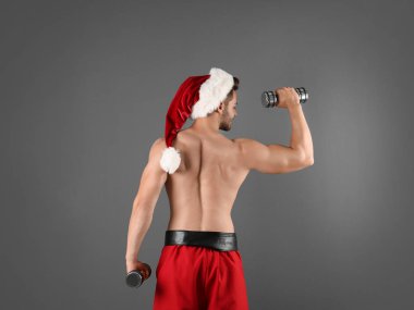 Gömleksiz seksi genç Noel Baba renk arka plan üzerinde dumbbells ile