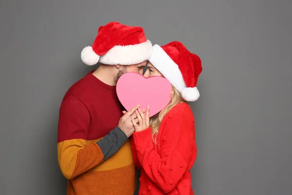 Pareja Joven Con Sombreros Santa Claus Escondidos Detrás Del Corazón —  Fotos de Stock