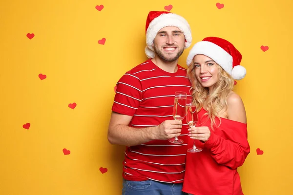 年轻夫妇在圣诞老人的帽子上 在彩色背景的香槟杯 圣诞庆典 — 图库照片