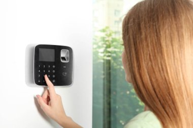 Young woman entering code on alarm system keypad indoors clipart