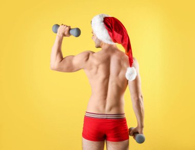 Gömleksiz seksi genç Noel Baba renk arka plan üzerinde dumbbells ile