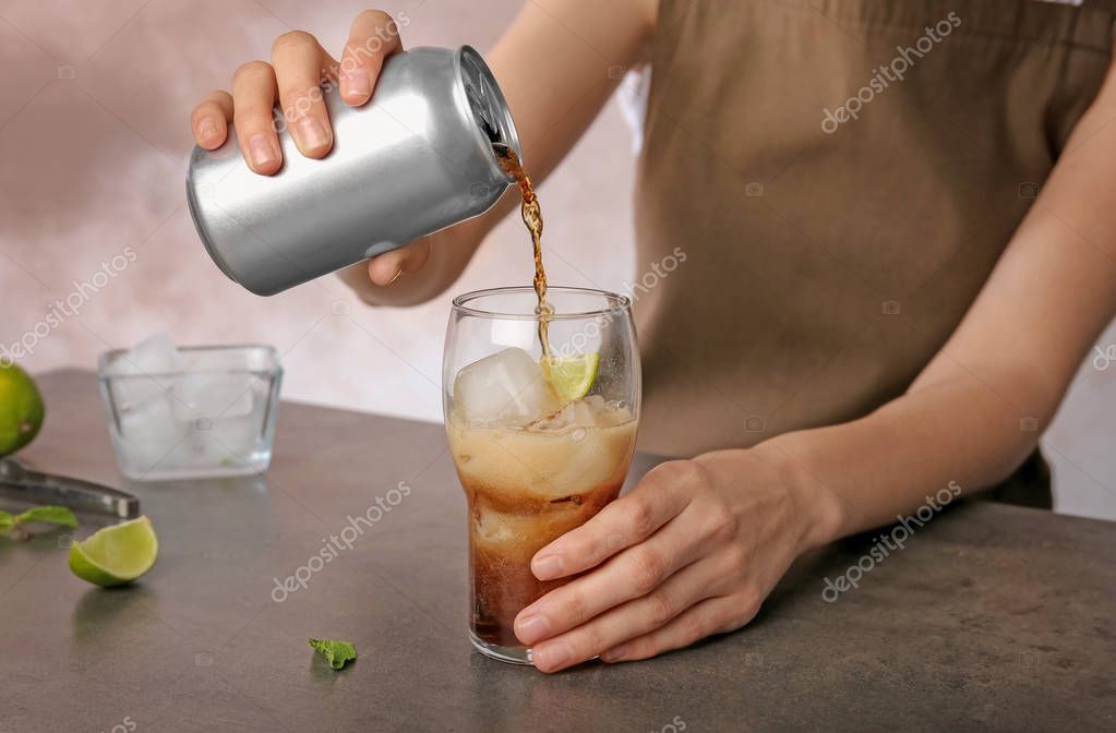 Woman pouring cola from tin can into glass at table