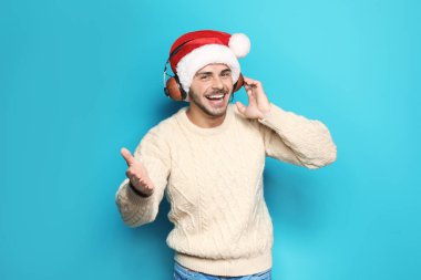 Genç adam Noel Baba şapkası renk arka plan üzerinde Noel müzik dinlemek