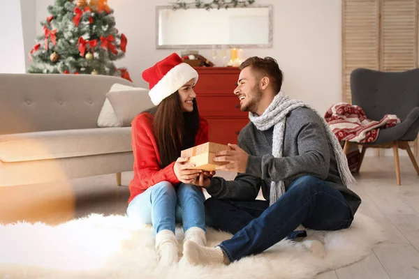 若い男は 自宅でガール フレンドにギフト ボックスを与えます クリスマスを祝う幸せなカップル — ストック写真