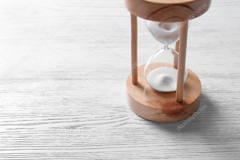 Hourglass with flowing sand on light wooden background. Time management