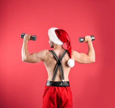 Gömleksiz seksi genç Noel Baba renk arka plan üzerinde dumbbells ile