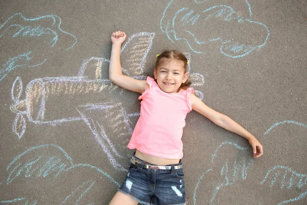 Little child lying near chalk drawing of airplane on asphalt, top view