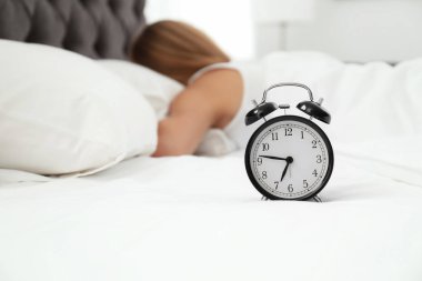 Analog alarm saat ve uykulu kadın yatakta. Günün saati