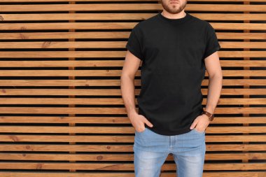 Sokakta ahşap duvar karşı siyah t-shirt giyen genç adam. Kentsel tarzı