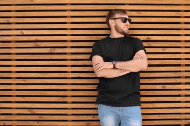 Sokakta ahşap duvar karşı siyah t-shirt giyen genç adam. Kentsel tarzı