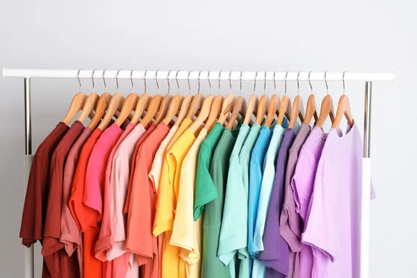 Rack with rainbow clothes on light background