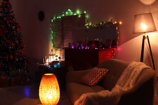 Stylish living room interior with Christmas tree and fairy lights at night