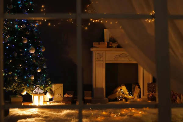 Stylish living room interior with decorated Christmas tree and fireplace at night, view through window