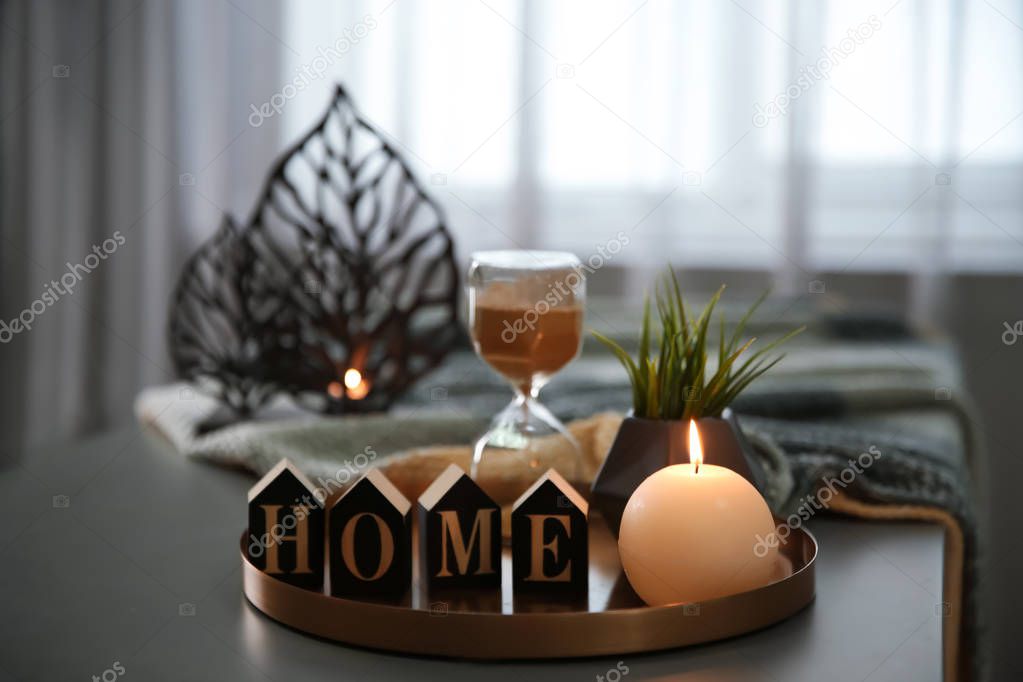 Tray with burning candle, word HOME and hourglass on table indoors