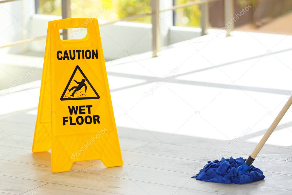 Safety sign with phrase Caution wet floor and mop, indoors. Cleaning service