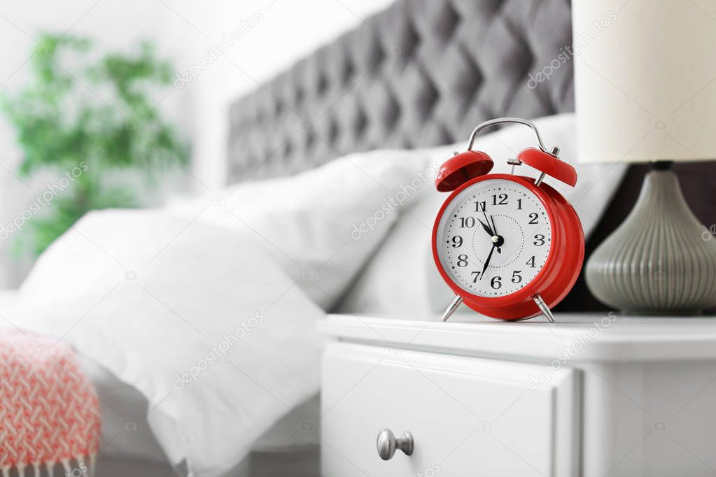 Analog alarm clock on table in bedroom. Time of day