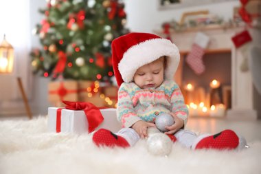 Şirin bebek evde kürk halıya oturup Noel Baba şapkalı. Noel kutlamaları