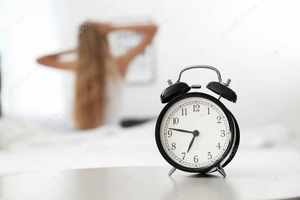Analog alarm clock and blurred woman on background. Time of day