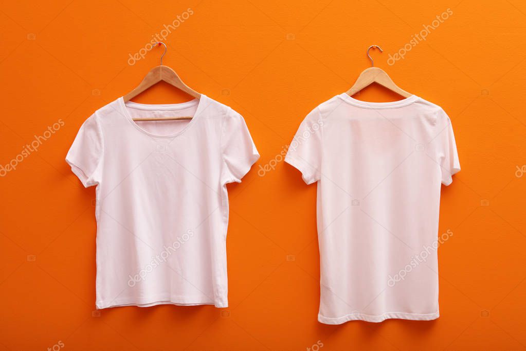 Hangers with blank t-shirts on color background. Mockup for design
