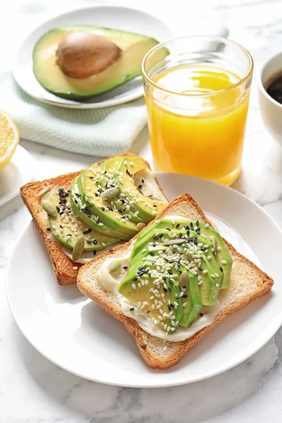 Toast bread with avocado and glass of juice on table