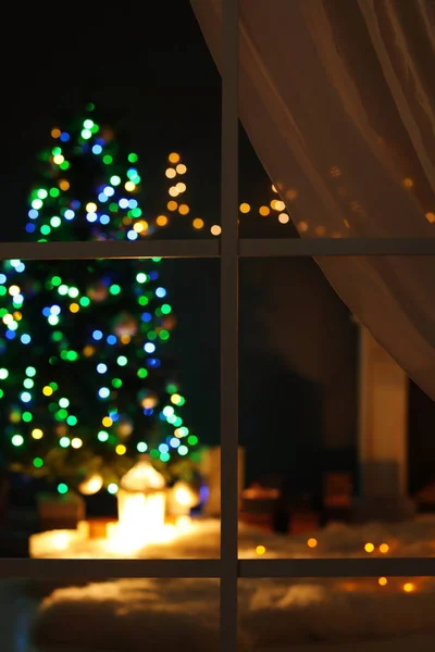 Blurred view of stylish living room interior with Christmas lights at night through window