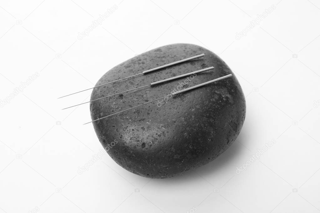 Acupuncture needles and stone on white background