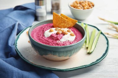Lezzetli pancar Humus, cips ve ahşap masa üzerine dilimlenmiş salatalık ile kase